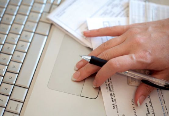 person holding a pen with a laptop and bills