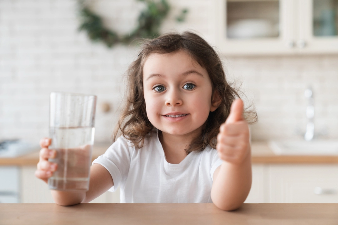 girl holding glass of water, giving thumbs up